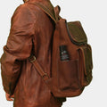 Side view of brown leather travel backpack showing a bottle in side pocket while a model in brown jacket posing