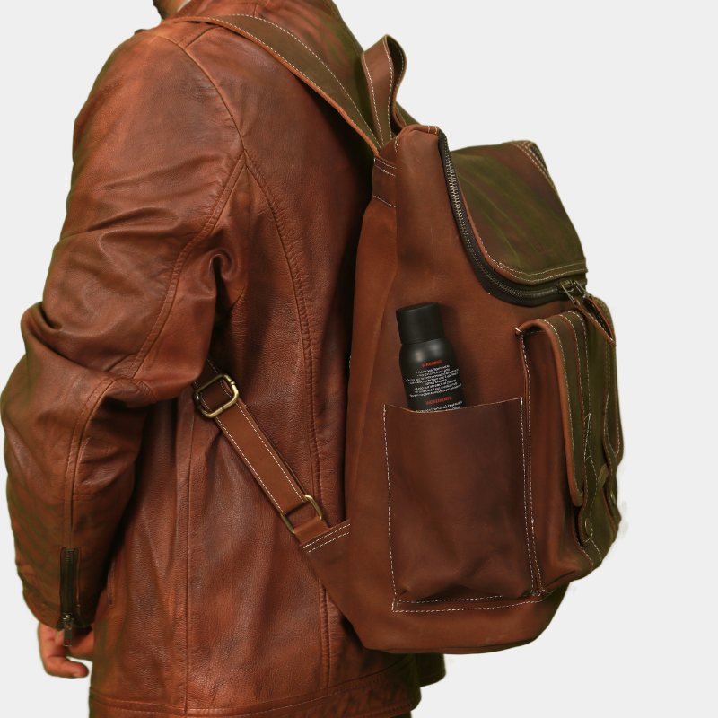 Side view of brown leather travel backpack showing a bottle in side pocket while a model in brown jacket posing