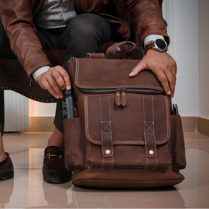Downtown Explorer Leather Backpack while a guy slipping a black bottle in side slip pocket