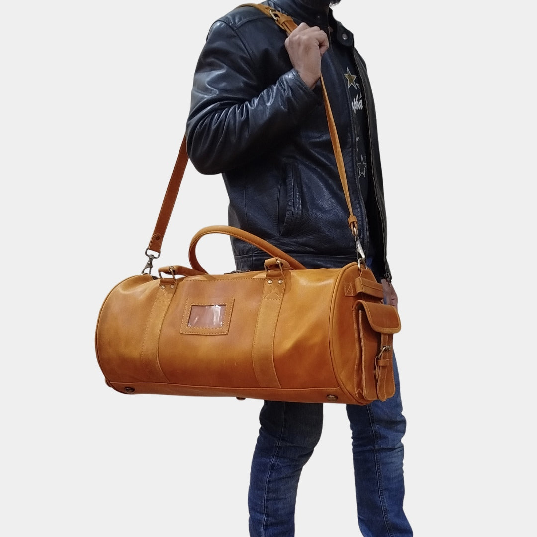 Guy in black jacket slinging brown costal duffle across shoulder using adjustable strap