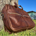 Dark Brown Messenger Bag for Men placed against a tree on grass 