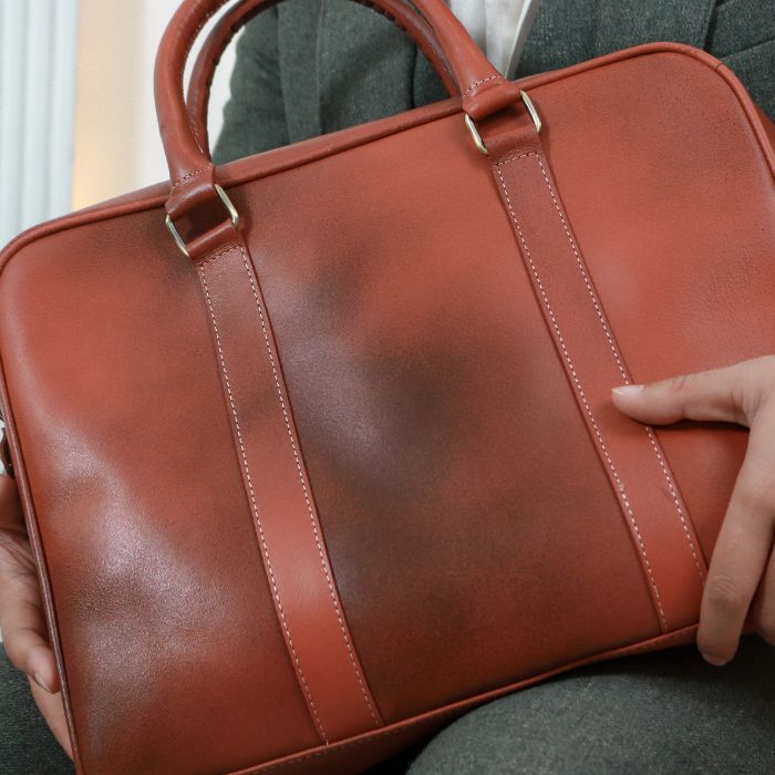 Model in Green suit posing with Commute King Leather Messenger bag in his hands while sitting on couch