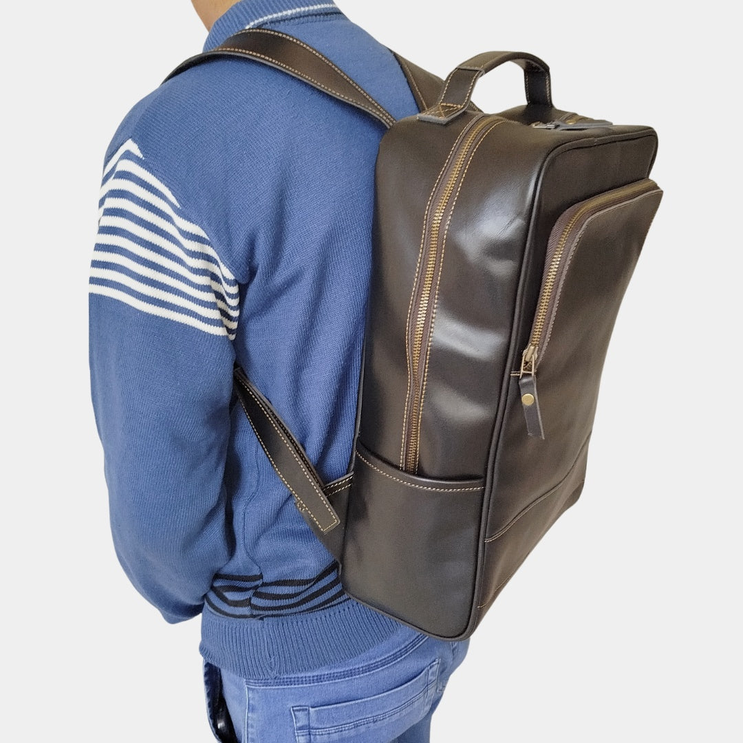 A model posing sideways with black leather backpack at his shoulder complementing a casual look in blue jeans and sweatshirt