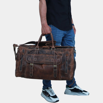 A model in black shirt and blue jeans holding Roma Leather Duffle bag using its soft grab handles