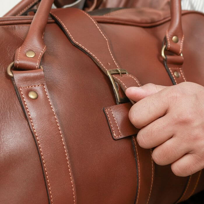 Guy opening front buckle strap of brown Leather duffle Bag by TLB Australia