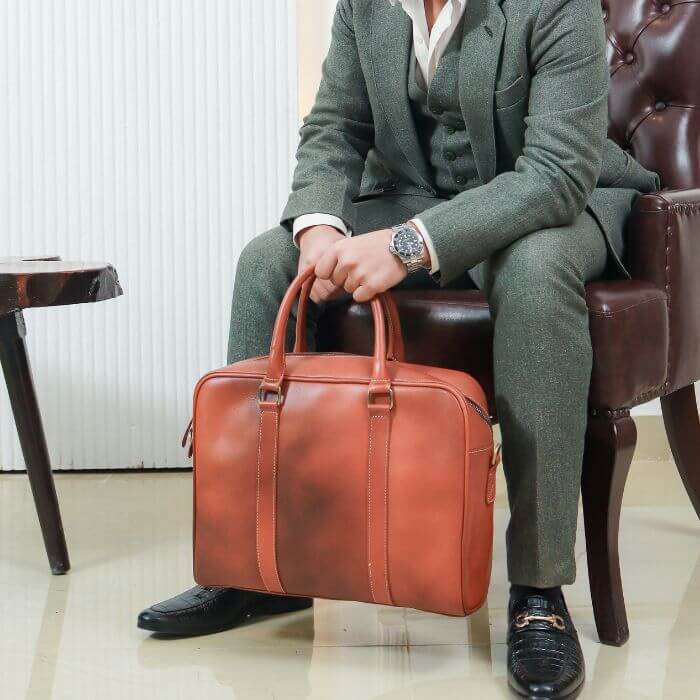 Model in Green suit posing with Commute King Leather Messenger bag in his hands while sitting on couch