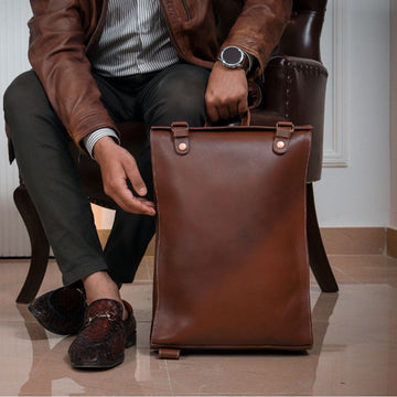 A guy sitting in chair posing High-quality leather Executive Edge backpack in classic brown, durable and versatile