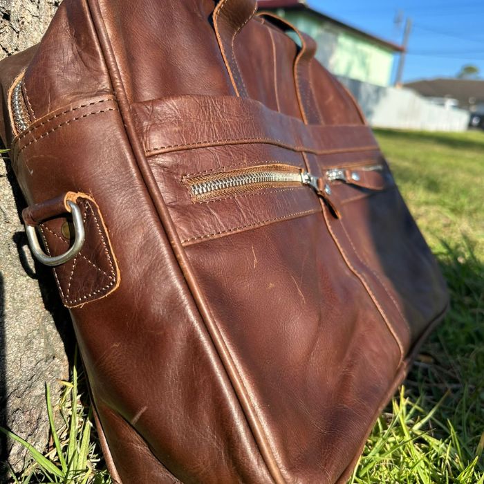 side view of The Tech Savvy Leather Messenger Bag placed on grass leaning against tree in outdoor setting of Australia 