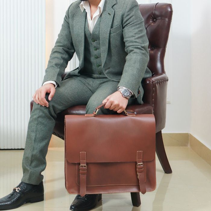 Model holding Business navigator Leather Messenger Bag in his hands sitting on sofa, perfect messenger bag for office