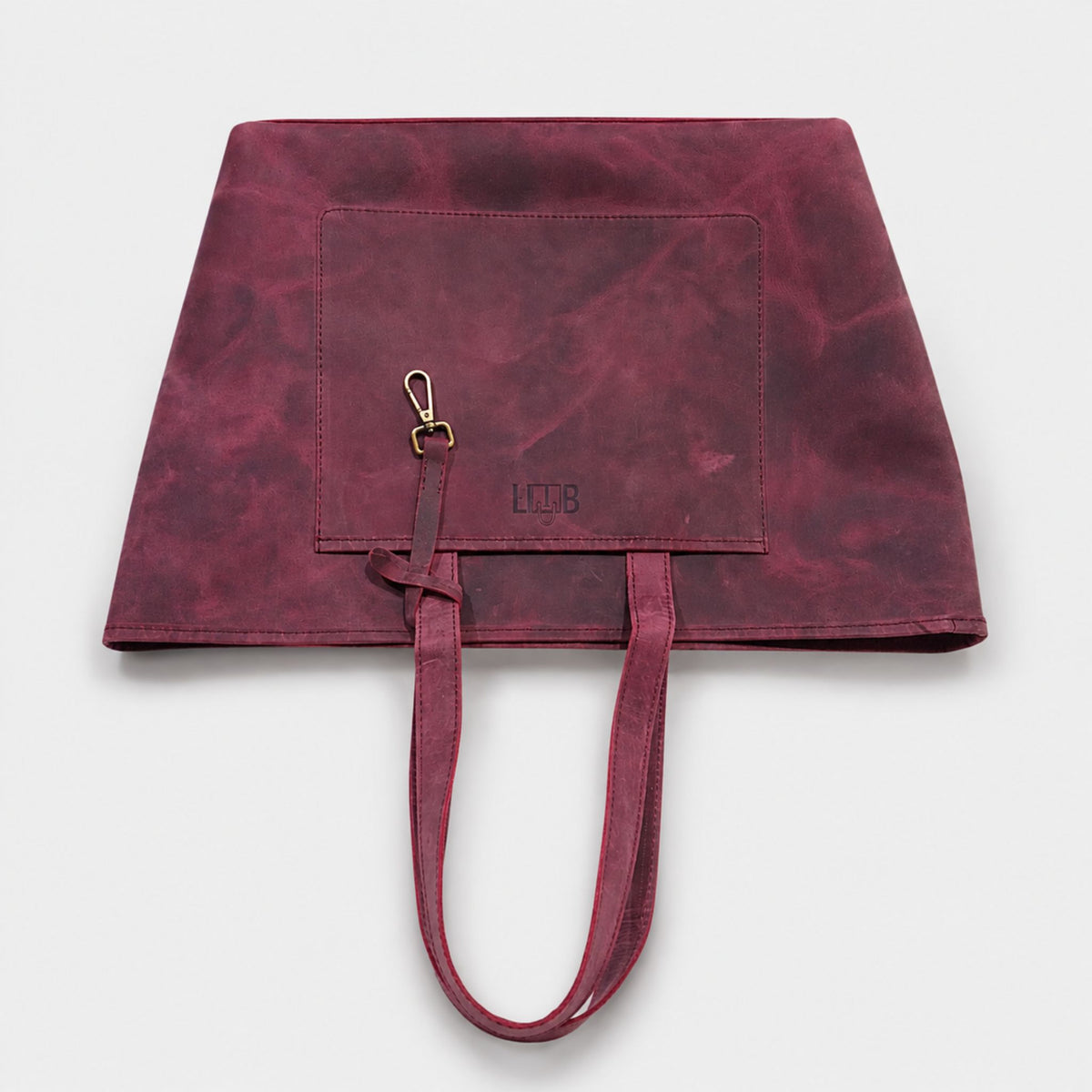 Top down view of a vintage burgundy genuine leather tote bag showing a large exterior front pocket and built-in key leash strap