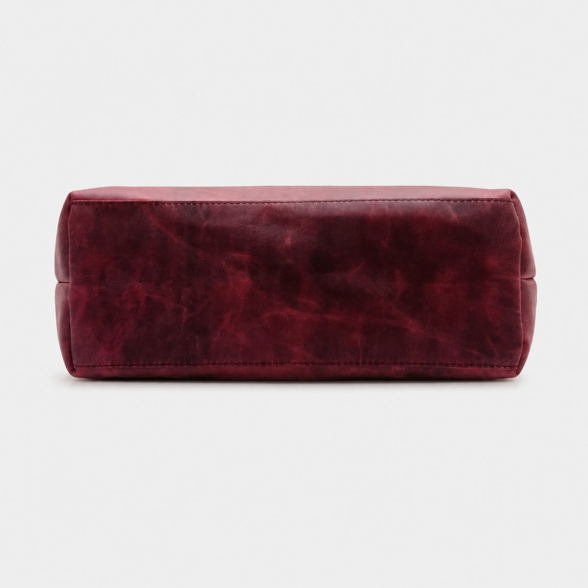Bottom view of a structured burgundy leather tote bag highlighting the thick perimeter stitching and a wide rectangular base for upright support