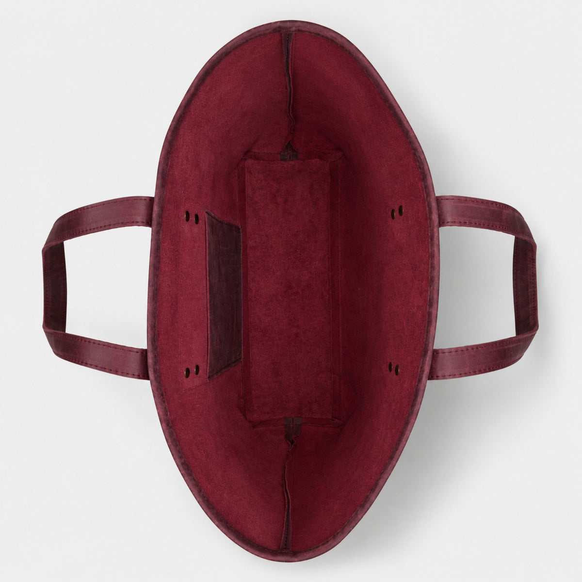 Interior layout of an unlined burgundy leather work bag showing the structural flat bottom panel and double rivet handle attachments